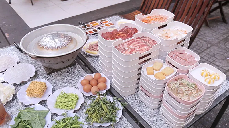 Không gian quán lẩu nướng với nhiều món ăn kèm và nước chấm